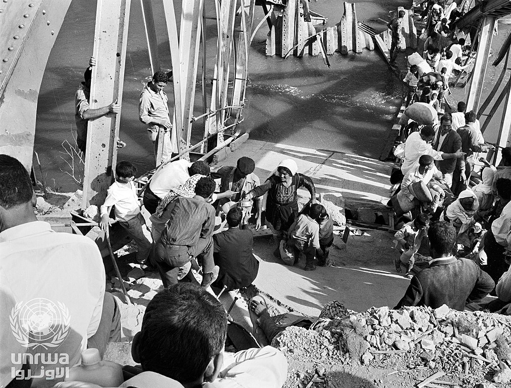 Palestine_refugees_flee_across_the_Allenby_Bridge_during_the_second_Arab-Israeli_hostilities_in_1967 Ihmisiä ylittämässä tavaroita kantaen siltaa, joka on osin uponnut.